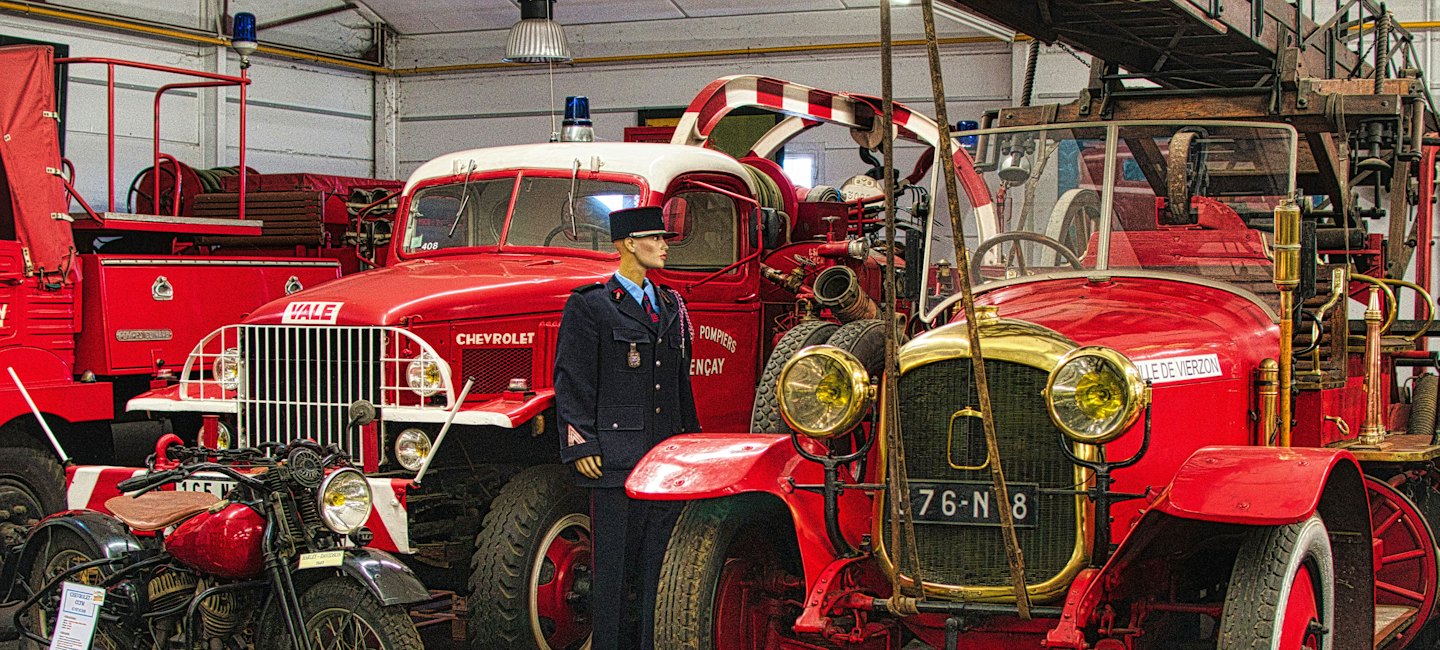 Eine Schaufensterpuppe in Feuerwehrmannsuniform steht zwischen alten Feuerwehrautos.