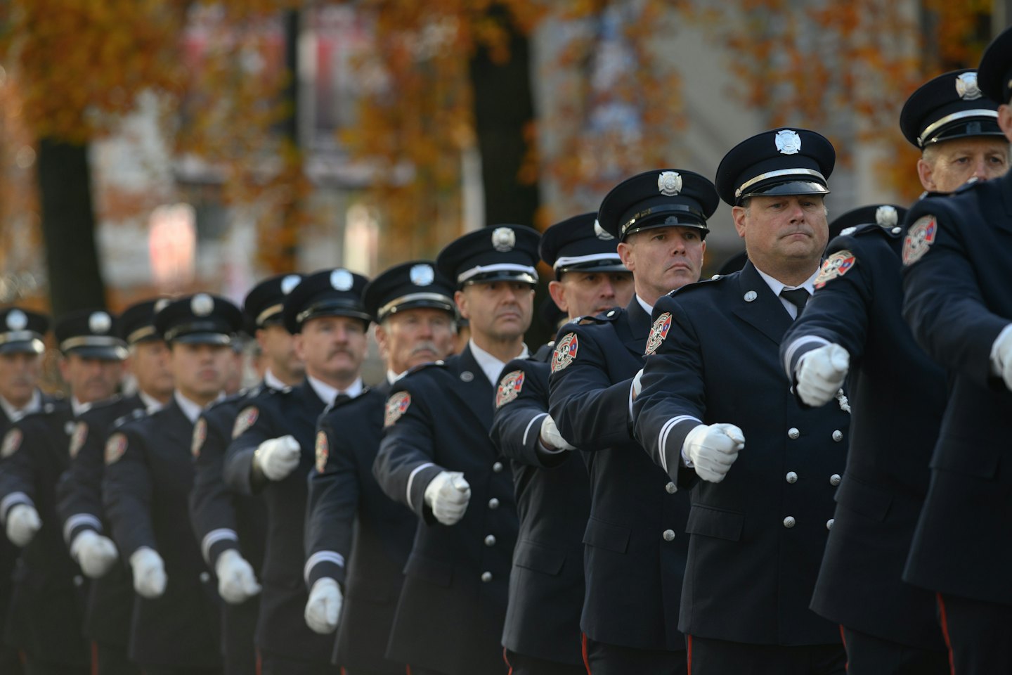 Feuerwehrleute in dunkelblauen Uniformen marschieren in einer feierlichen Parade.