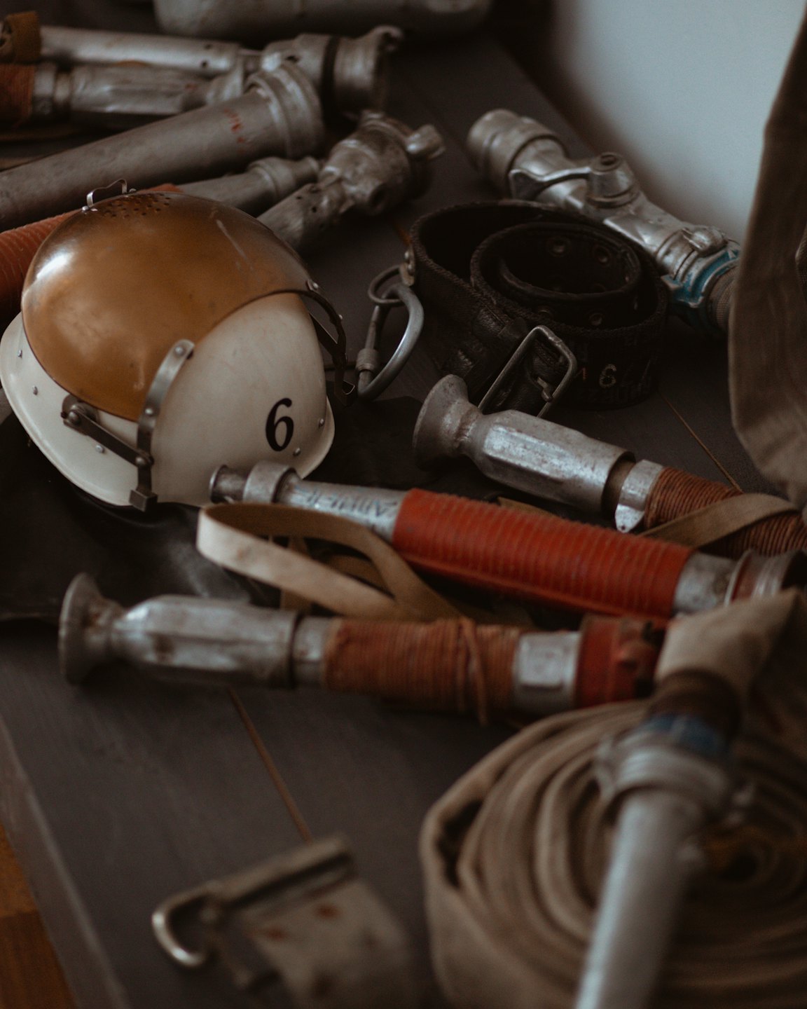 Alter Feuerwehrhelm, Schlauchleitungen und Metallausrüstung auf Holz.